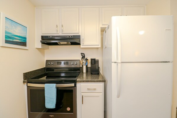 A compact kitchen with white cabinets, a stainless steel oven, a white refrigerator, and a granite countertop.