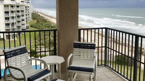 Een balkon met twee witte stoelen en een kleine tafel, met uitzicht op een strand en zee.
