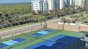 Een tenniscomplex met meerdere banen, omheind door een hek, grenzend aan een parkeerplaats.