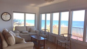 Una sala de estar con un sofá, sillas, una mesa de centro y ventanas amplias con vista a la playa y al océano.