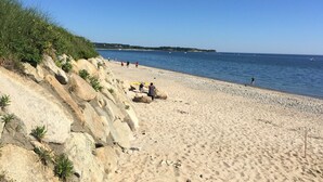 Una playa arenosa con terreno rocoso y vegetación escasa.