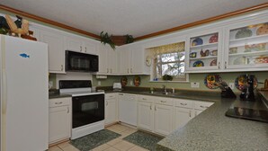 Una cocina con gabinetes blancos, microondas, estufa y lavaplatos.