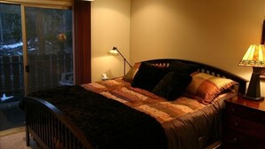 Ein Schlafzimmer mit einem Bett, einem Nachttisch, einer Lampe und einer Schiebetür, die auf einen Balkon führt.