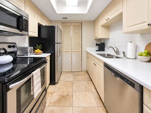 Een moderne keuken met een ingebouwde oven, magnetron en vaatwasser, met een lichtgekleurde tegelvloer en een dakraam boven het aanrecht.