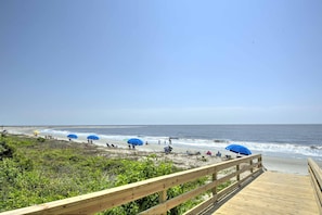 Walk along the beach to the shore, where umbrellas provide shade and the ocean's waves gently approach.