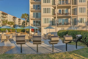 Experience the hotel's modern design, featuring spacious balconies and outdoor seating areas with tables and chairs, amidst lush greenery and palm trees.