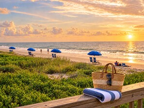 A beach scene with a wooden deck, a woven basket, and a folded towel.