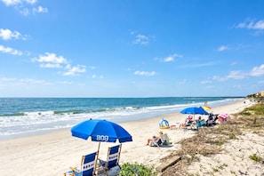 Une plage avec un ciel dégagé, un rivage sablonneux et plusieurs parasols bleus.