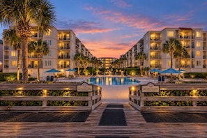 A resort with a central pool, multiple balconies, and a wooden boardwalk leading to the pool. - Beautiful Ocean Views, Beach Club 337! Steps to beach! (St. Simons Island)