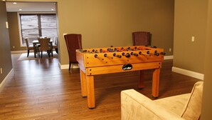 A room with a wooden foosball table, a dining table with chairs, and a sofa.