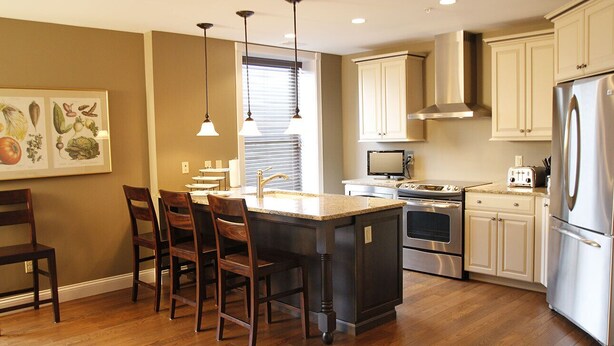 A kitchen with a central island, dark cabinetry, stainless steel appliances, and a dining area with wooden chairs.