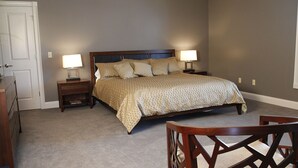 A bedroom with a large bed, two bedside tables with lamps, a wooden chair, and a door.