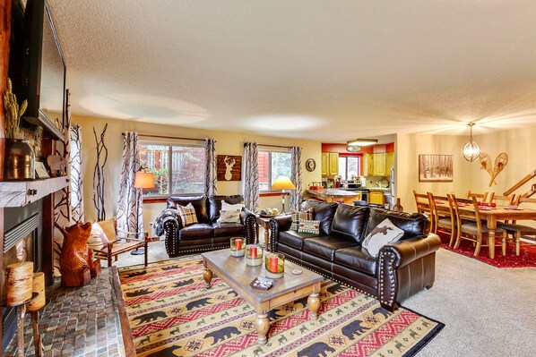 A cozy living room with a fireplace, a dining area with a wooden table and chairs, and a kitchen in the background. - Pine Ridge Ski-In Condo on Four O'Clock Ski Run - 1 block from Downtown (Breckenridge)