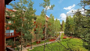 A courtyard with a lawn, trees, and a red building with balconies. - Pine Ridge Ski-In Condo on Four O'Clock Ski Run - 1 block from Downtown (Breckenridge)