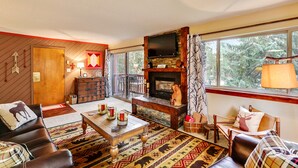 A cozy living room with a fireplace, leather furniture, and a large window offering a view of trees. - Pine Ridge Ski-In Condo on Four O'Clock Ski Run - 1 block from Downtown (Breckenridge)