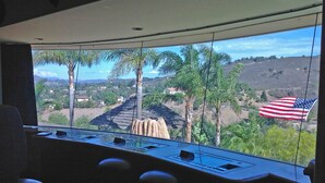 Ein Kontrollraum mit einem großen Fenster, das einen Blick auf eine Landschaft mit Palmen und eine Anhöhe mit Häusern bietet.
