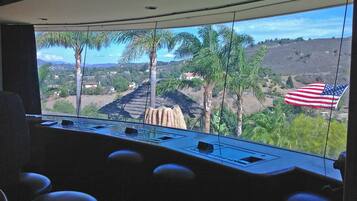 A control room with a large window overlooking a landscape with palm trees and a view of a hill with houses.