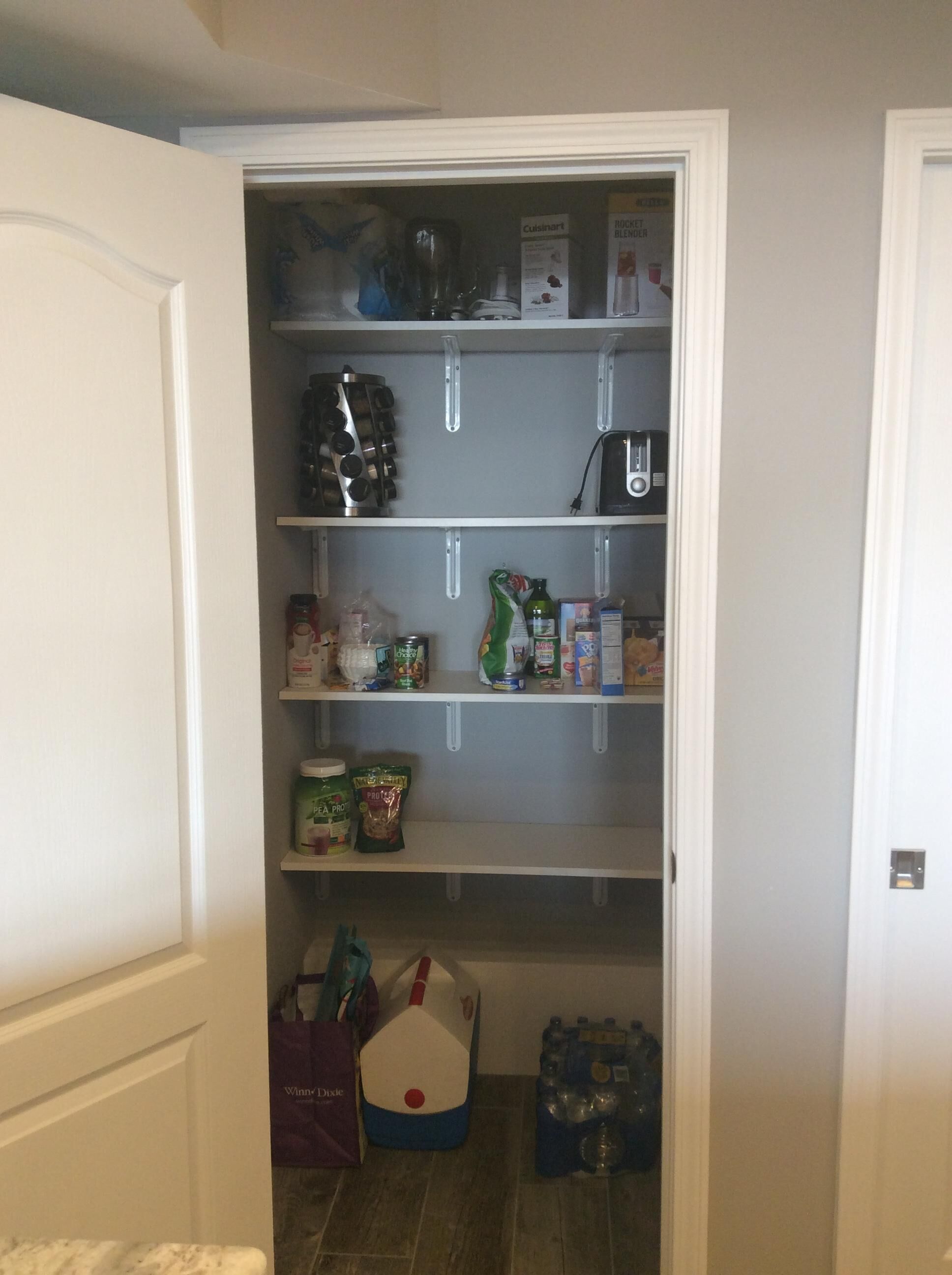 A pantry with shelves stocked with various food items, a coffee maker, and a blender.