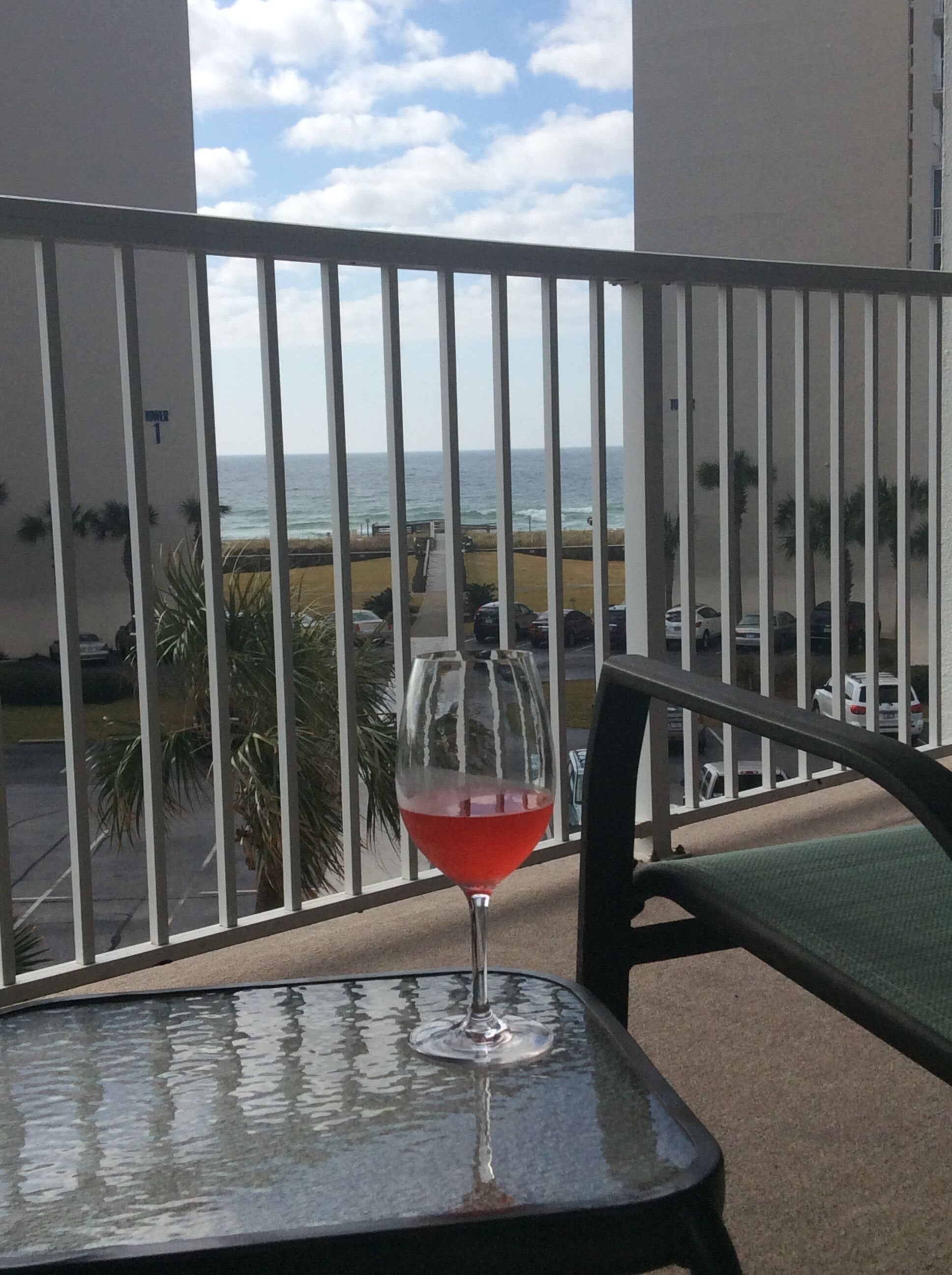 A balcony with a table and a glass of red wine, overlooking a beach and ocean.