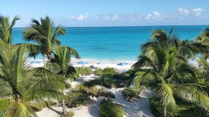 Una spiaggia con sabbia bianca, palme e ombrelloni blu.