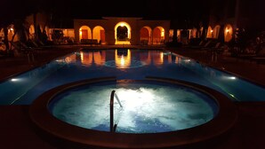 Una piscina con una vasca idromassaggio al centro, circondata da poltroncine e un edificio ad arco sullo sfondo.