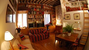 Una sala de estar acogedora con techo de madera, un sofá a rayas, una mesa de comedor con sillas y una estantería llena de libros.