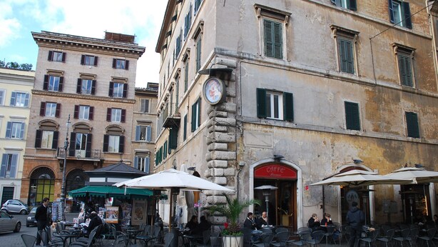 Un café al aire libre con mesas en la terraza y un edificio de piedra al fondo.