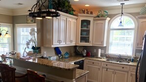 A kitchen with white cabinetry, a granite countertop, and a bar area with two wooden chairs. - Gorgeous 5 bdrm OCEAN LAKES FAMILY CAMPGROUND MH137C (Myrtle Beach)