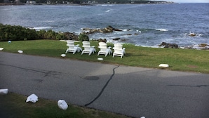A coastal view with white chairs on a grassy area beside a road, overlooking the sea and a distant shoreline with houses. - Gorgeous 6 Bedroom Ocean Front Home steps from Short Sands (York)