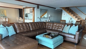 A spacious living room with a large brown sectional sofa, a light blue ottoman, and a wooden floor. - Gorgeous 6 Bedroom Ocean Front Home steps from Short Sands (York)