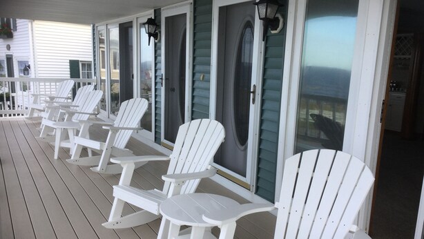 A covered outdoor seating area with white Adirondack chairs and a table, overlooking a body of water. - Gorgeous 6 Bedroom Ocean Front Home steps from Short Sands (York)