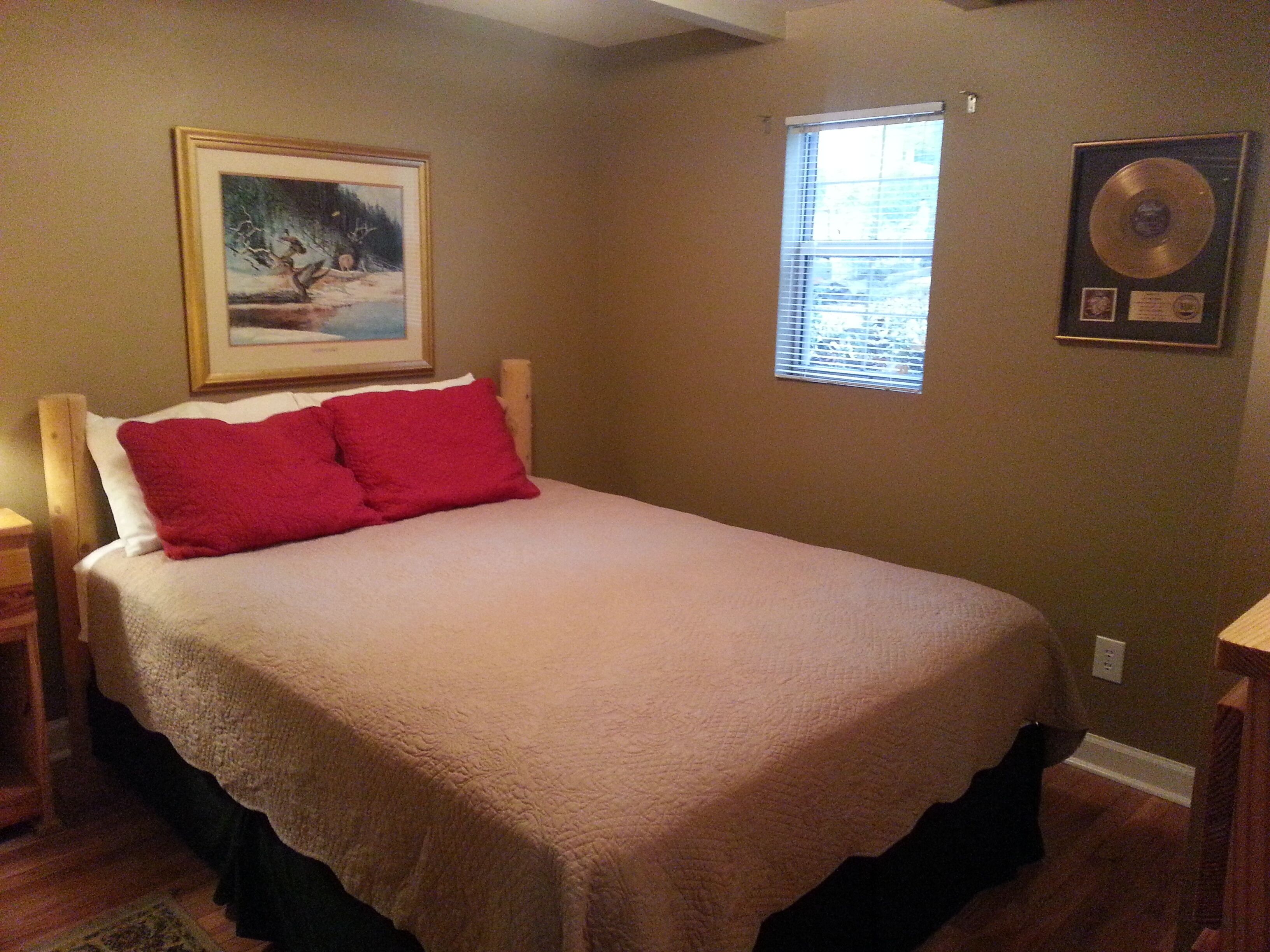 A bedroom with a bed, a framed picture on the wall, a window, and a framed award on the wall.