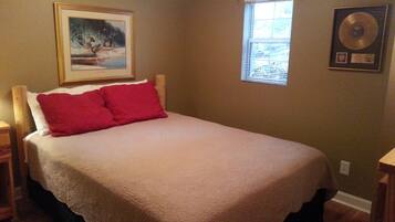 A bedroom with a bed, a framed picture on the wall, a window, and a framed award on the wall.