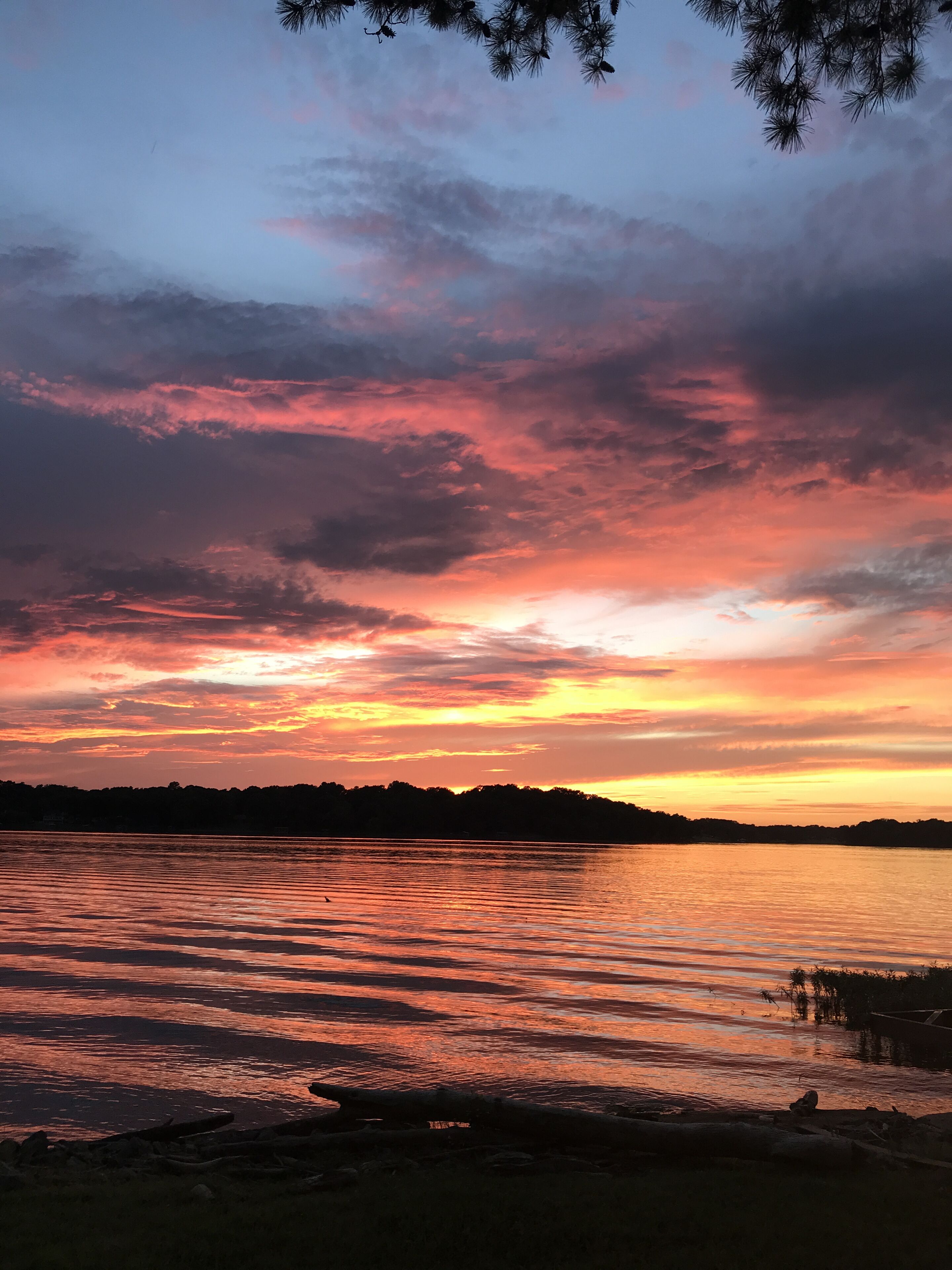 A sunset over a calm lake with a silhouette of trees and a dock.