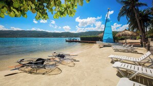A beach with clear water, lounge chairs, and a sailboat. - Beach Front Villa W/Pool/Staff, in Gated Community W/Tennis/Gym (Montego Bay)