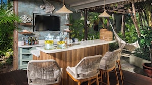 A bar area with a wooden counter, wicker chairs, and a television mounted on the wall. - Beach Front Villa W/Pool/Staff, in Gated Community W/Tennis/Gym (Montego Bay)