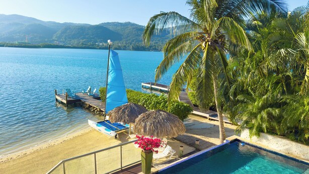 A poolside area with lounge chairs, a small sailboat, and a view of the water. - Beach Front Villa W/Pool/Staff, in Gated Community W/Tennis/Gym (Montego Bay)