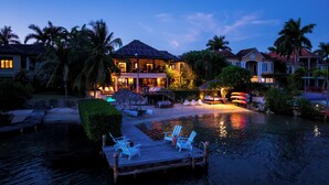 A waterfront property with a dock, lounge chairs, and a swimming pool. - Beach Front Villa W/Pool/Staff, in Gated Community W/Tennis/Gym (Montego Bay)