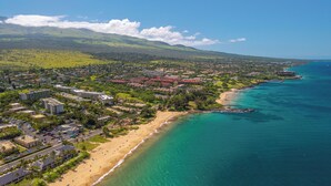 Vue aérienne d’une ville côtière avec une plage, des quartiers résidentiels et une chaîne de montagnes en arrière-plan.
