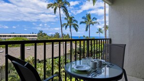 Un balcon avec une table dressée pour deux personnes, offrant une vue sur des palmiers et un immeuble.