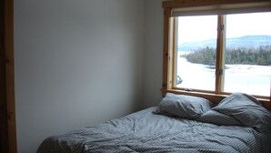 Cama de casal com roupa de cama listrada num quarto com uma janela grande com vista para a água e árvores.
