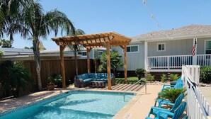 A swimming pool with a wooden pergola, lounge chairs, and a white fence. - The Pool House located in Coveted Old Town with Pool (Port Aransas)
