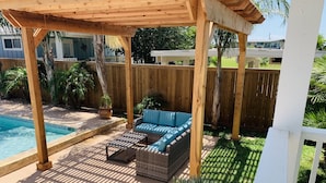 A covered patio area with a pool, wooden deck, and outdoor furniture. - The Pool House located in Coveted Old Town with Pool (Port Aransas)