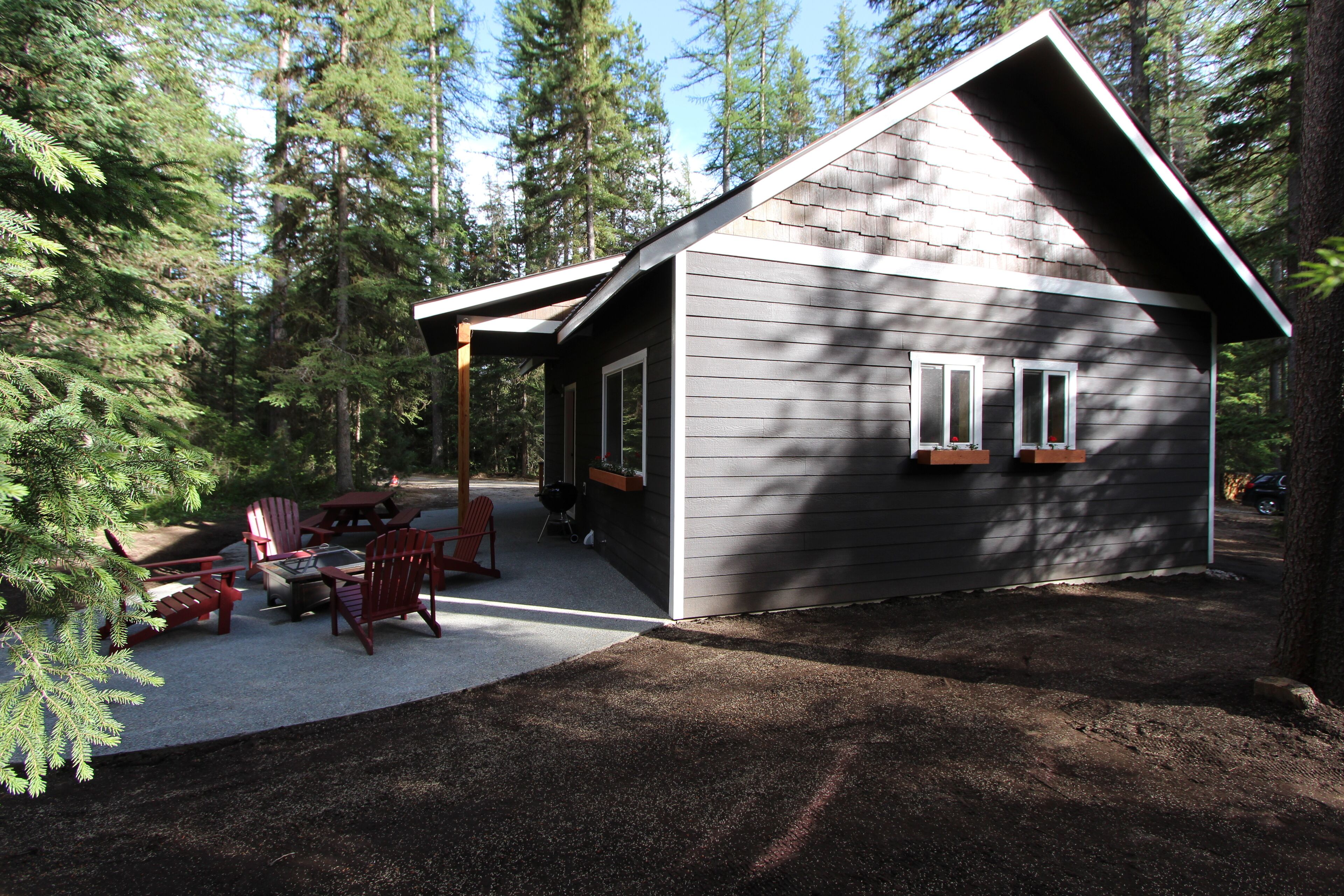 A cabin with a covered patio, outdoor seating, and a view of the surrounding forest.