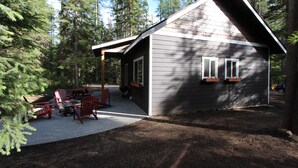 A cabin with a covered patio, outdoor seating, and a view of the surrounding forest.