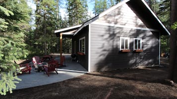 A cabin with a covered patio, outdoor seating, and a view of the surrounding forest.