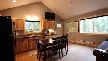 A kitchen with wooden cabinets, a dining table with chairs, a refrigerator, and a window with a view of trees.