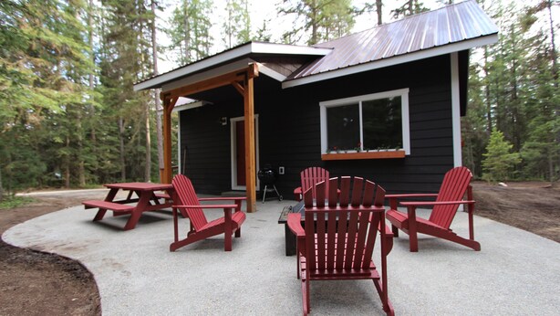 A cabin with a covered patio area, two Adirondack chairs, and a picnic table.