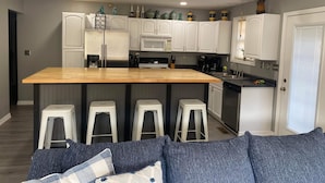 A modern kitchen with white cabinets, a wooden island with bar stools, and a built-in oven.