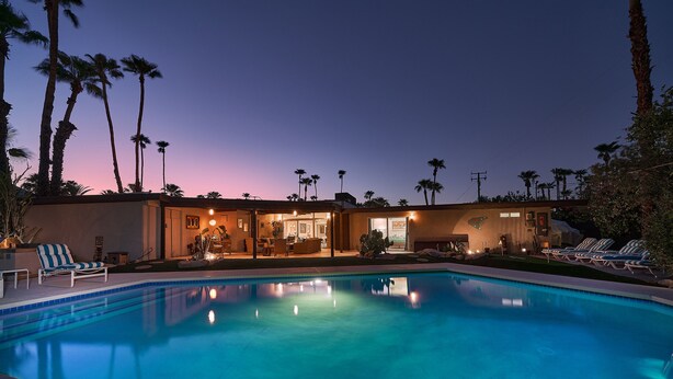 A swimming pool with lounge chairs, a building with multiple rooms, and palm trees.